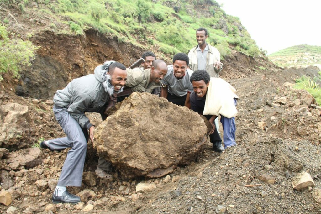 A group of men moving a boulder to clear the path for a new road