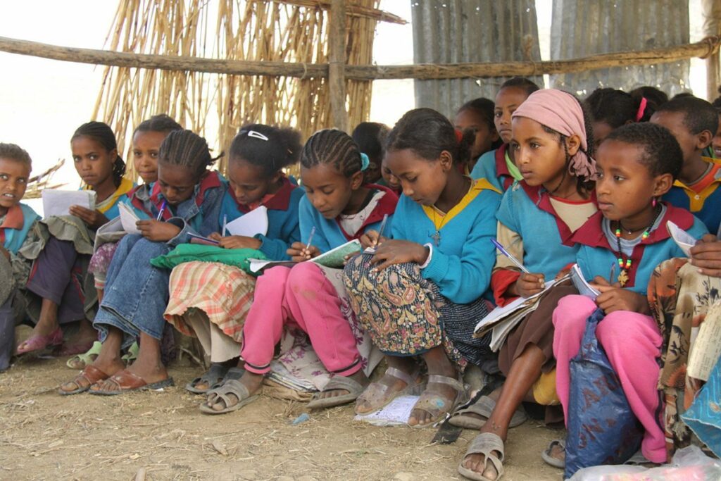 Ethiopian school children writing in exercise books in an open air classroom