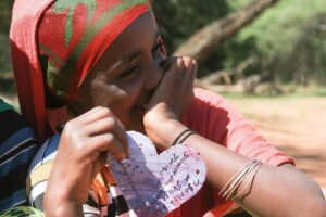 A young Ethiopian girl smiling while holding a heart shaped cutout