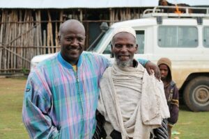 Amaha standing with his arm around community elder in Ganzilla.