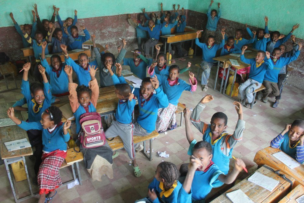 Children at desks with hands raised.